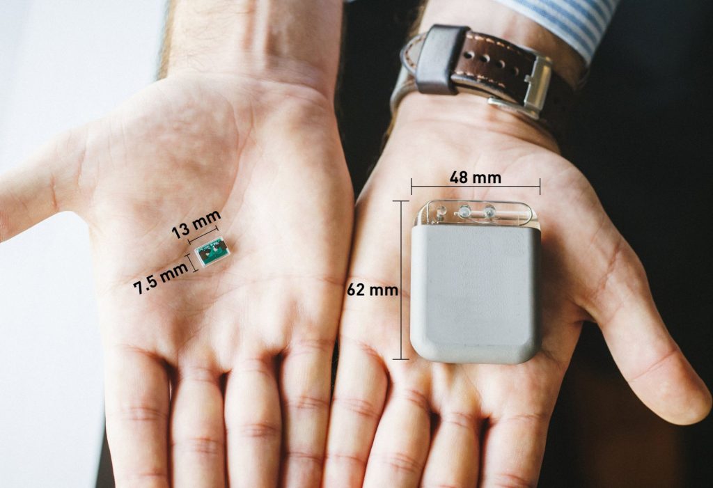 A person's hand holding two different medical devices for comparison